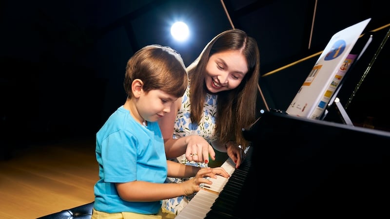 A piano teacher guiding her student, a young boy on how to play the piano.