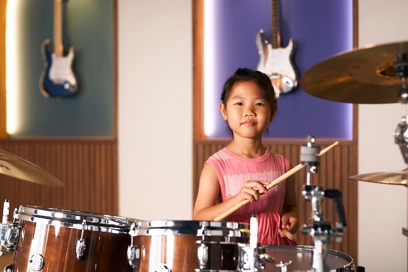 A female student in a music studio is practicing on a drum set.