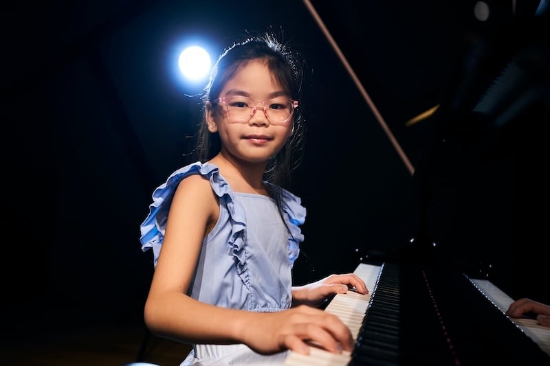 Aureus Academy piano student, Bella, smiling at the camera as she plays the piano.
