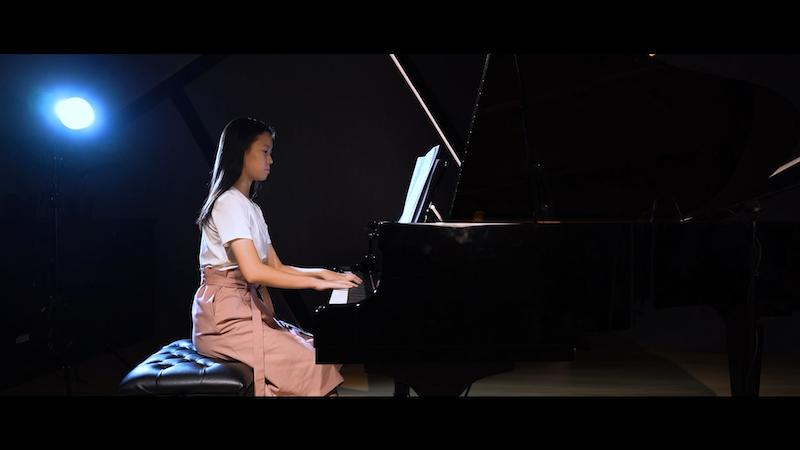 A teenage girl playing the grand piano in a recital hall.
