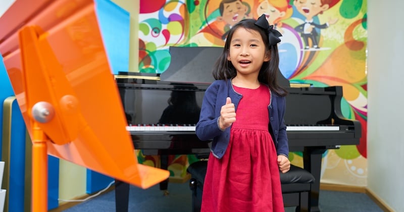 A young student attending music class. She is giving a thumbs up.