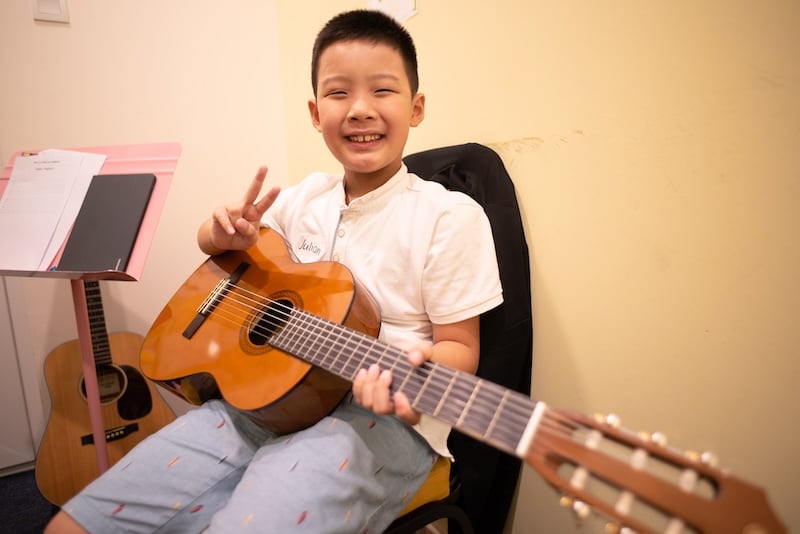 Student holding guitar and smiling with a peace sign.