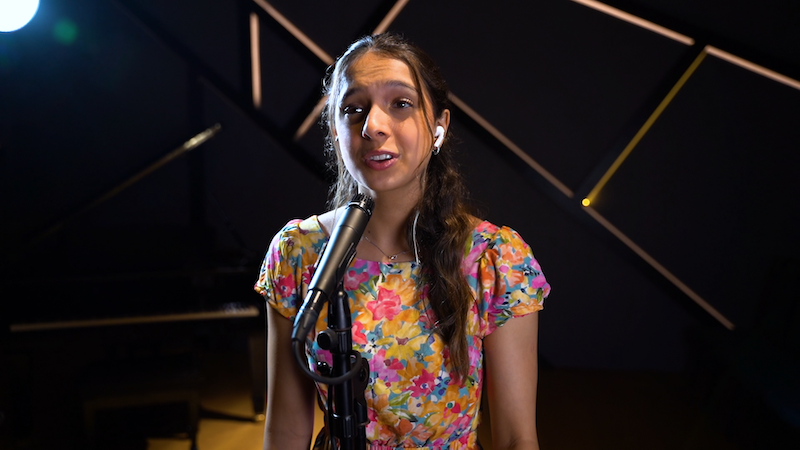 An Aureus voice student in a floral dress singing into the microphone in front of her.